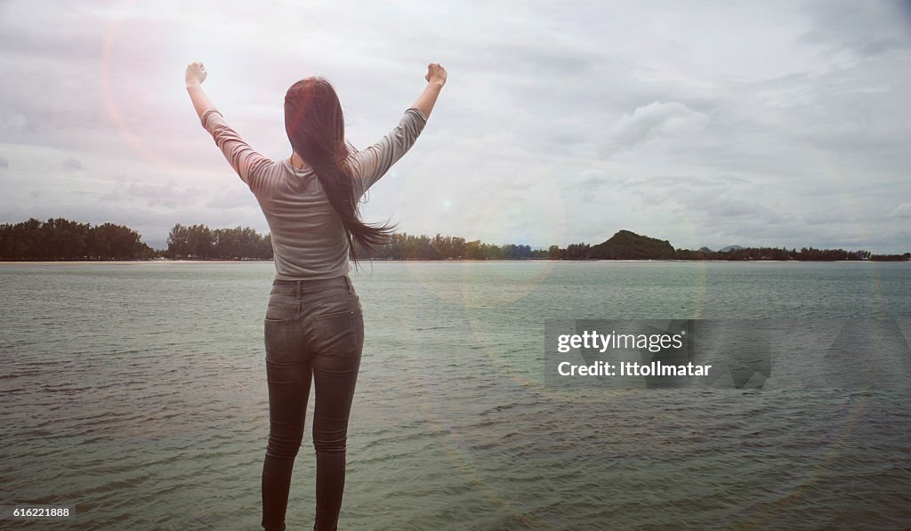 Woman standing on a cliff raising arms towards