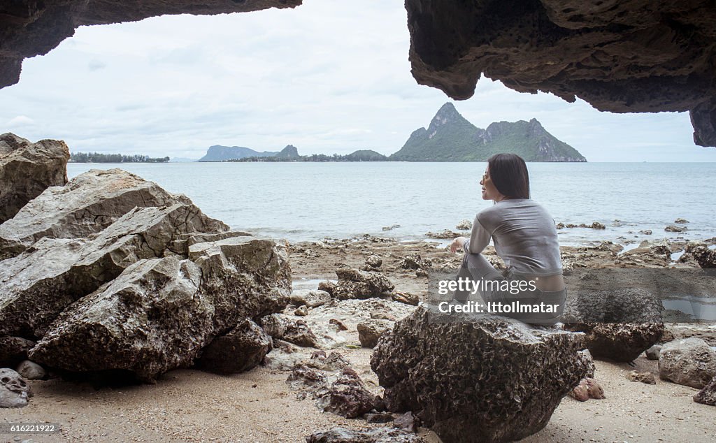 Happy young asian woman sitting on a rock