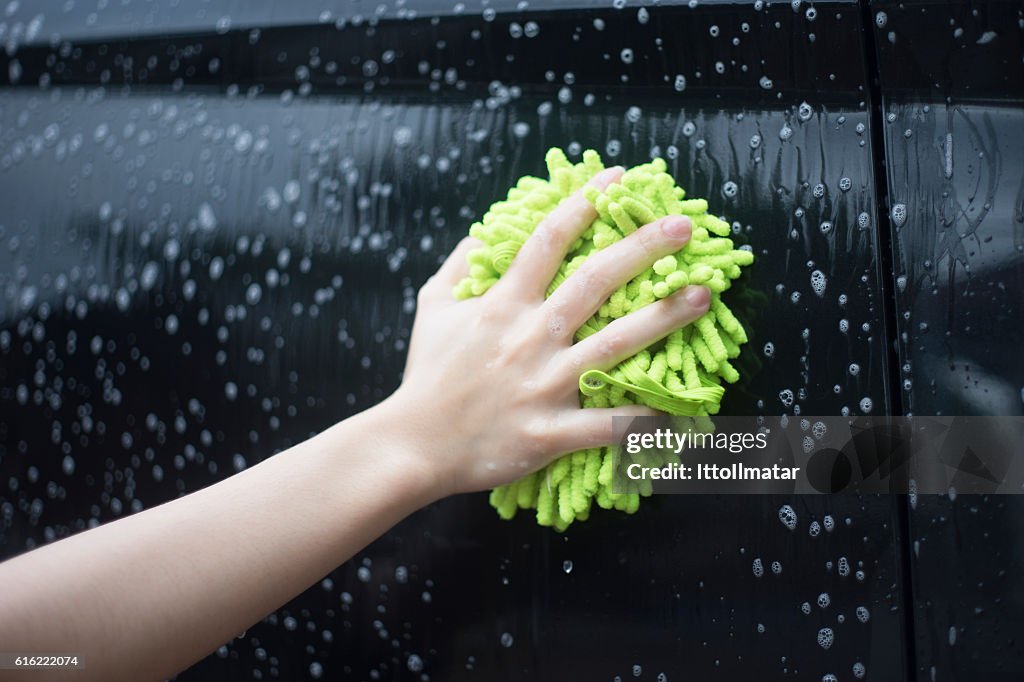 Woman hand hold a brush washing over the black car