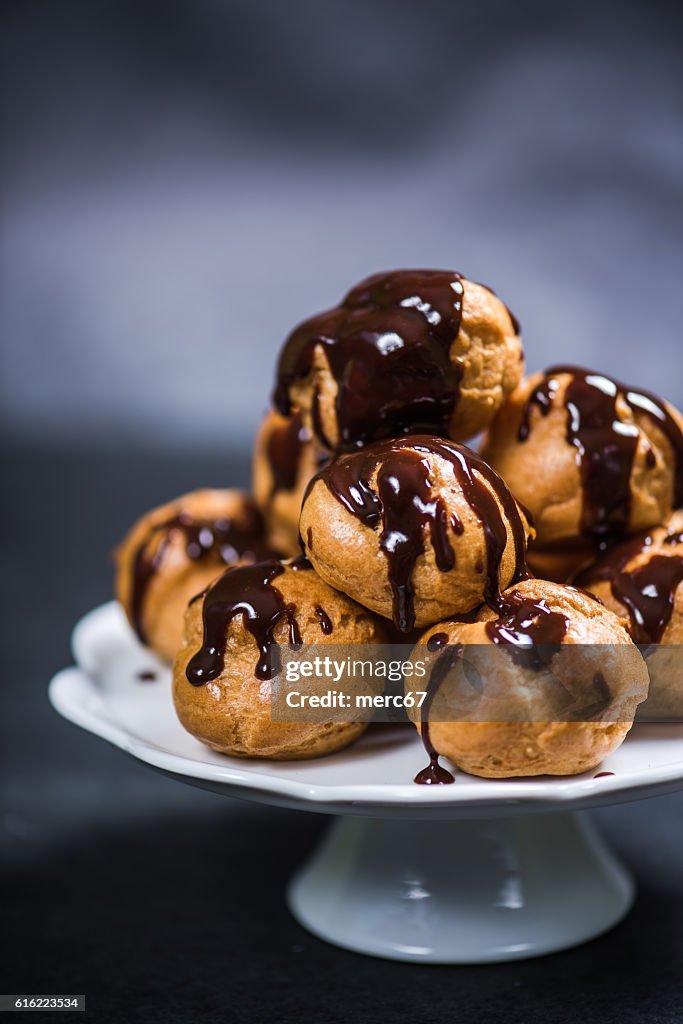 Stack of profiteroles eclairs with dark melted chocolate