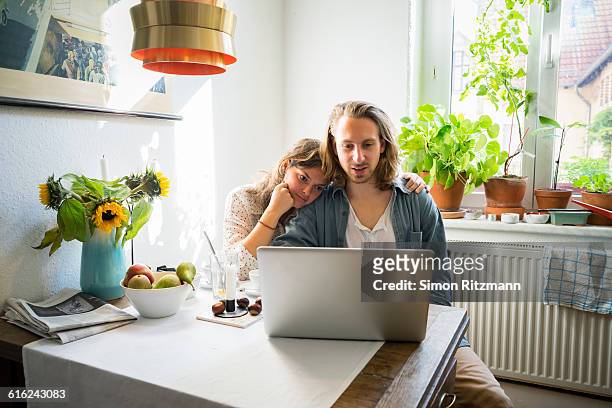 young couple using laptop in kitchen - young couple fotografías e imágenes de stock