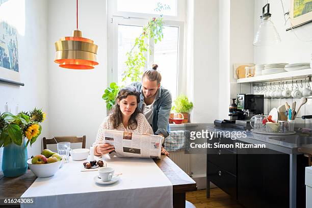 young couple reading newspaper in kitchen - news 2015 stock pictures, royalty-free photos & images