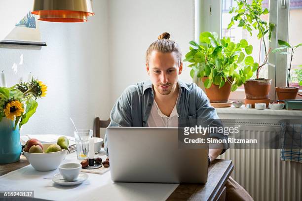 handsome young man using laptop in kitchen - working from home stock-fotos und bilder