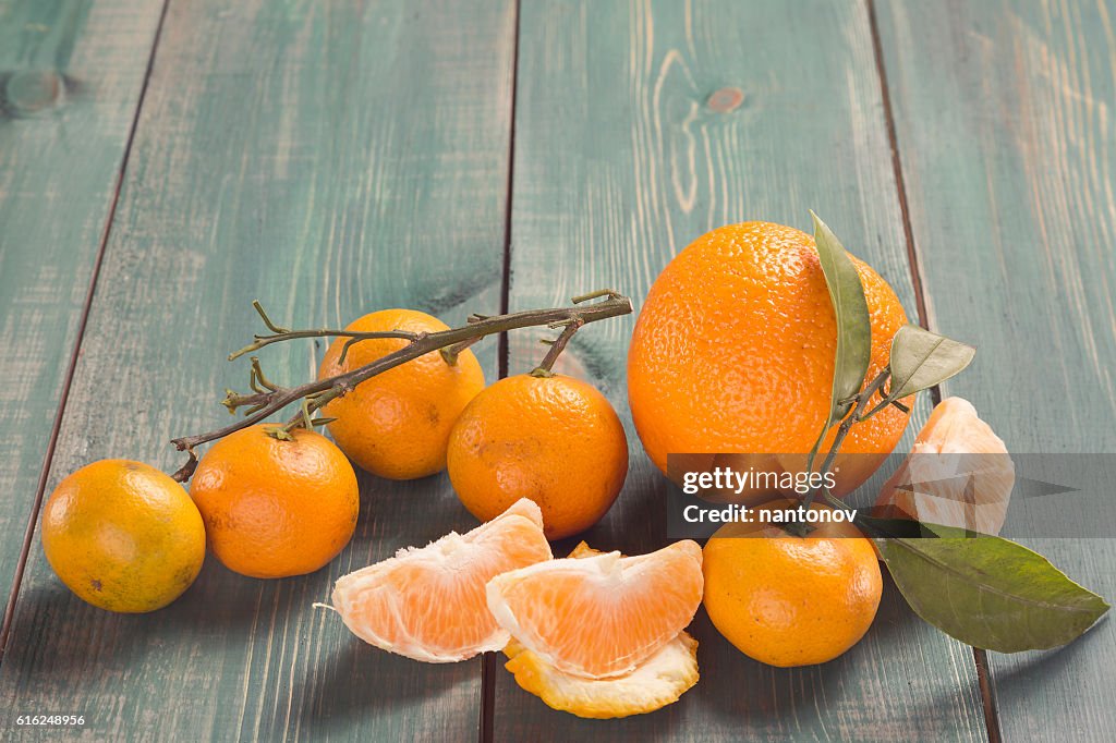 Tangerines with branch, leafs and orange slices on green wooden