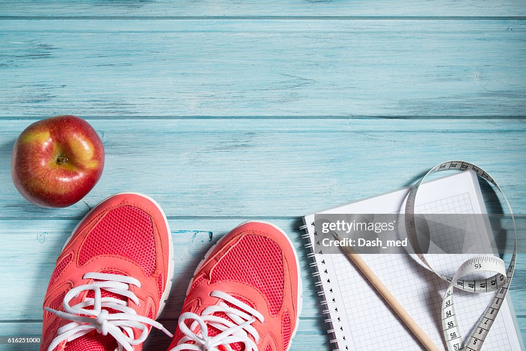 Fitness concept, pink sneakers, apple and notebook and measuring tape