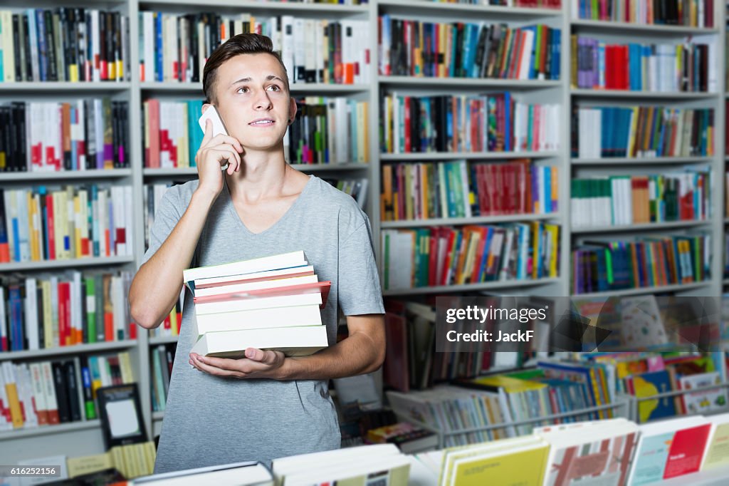 Boy holding books and talking on mobile phone in shop