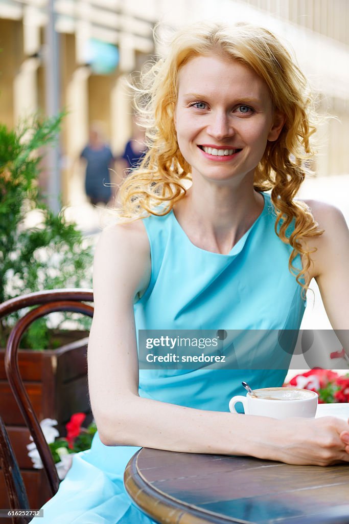 Sorridente giovane donna bionda al bar con tazza di cappuccino