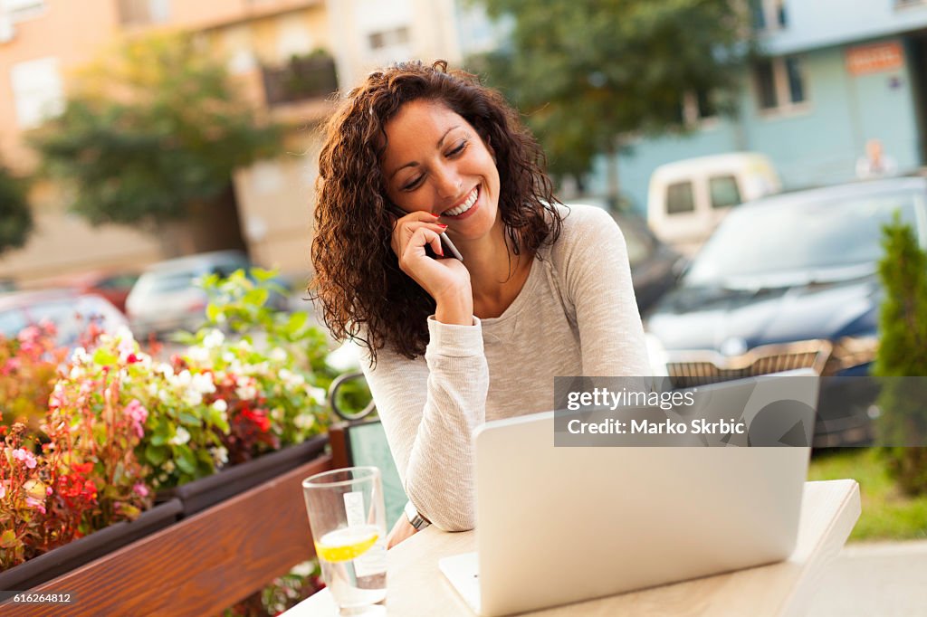 Smiling woman using laptop and talking on the phone