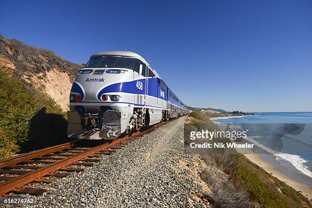 Amtrak Surfliner passenger train on tracks running alongside Pacific Ocean beaches near Santa Barbara on the west coast of California, USA