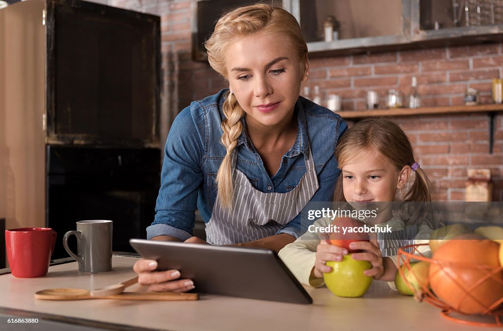 Nettes Mädchen lesen Rezepte mit ihrer Mutter in der Küche
