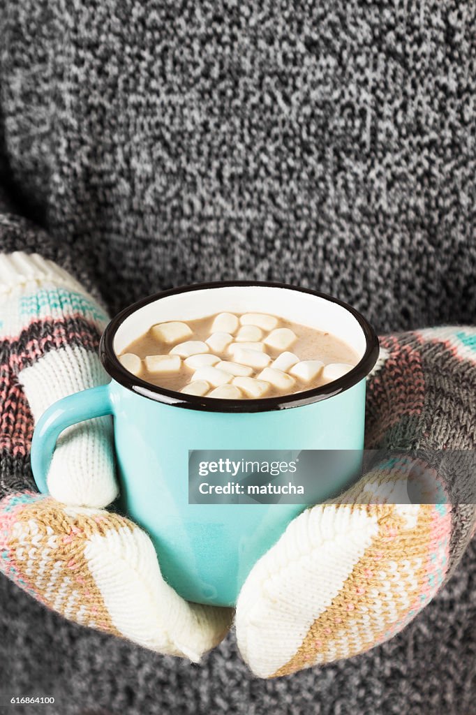 Girl keeps a mug of cocoa with marshmallows in mittens