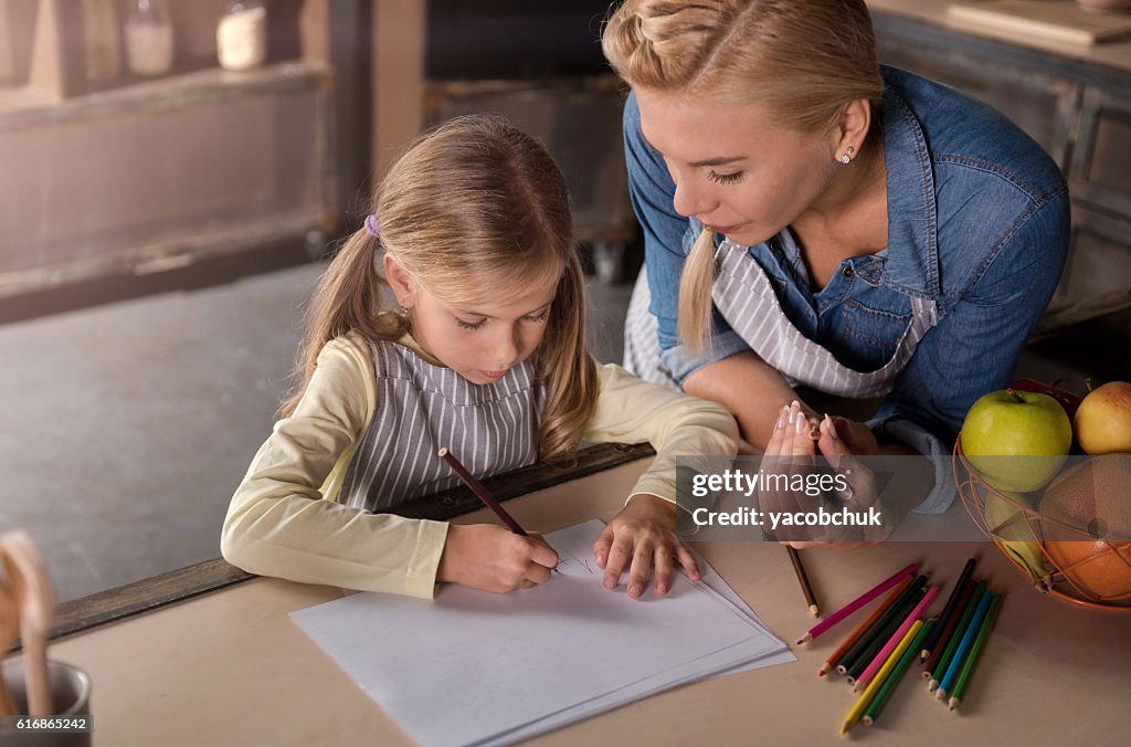 Madre encantada dibujando con su hija en la cocina