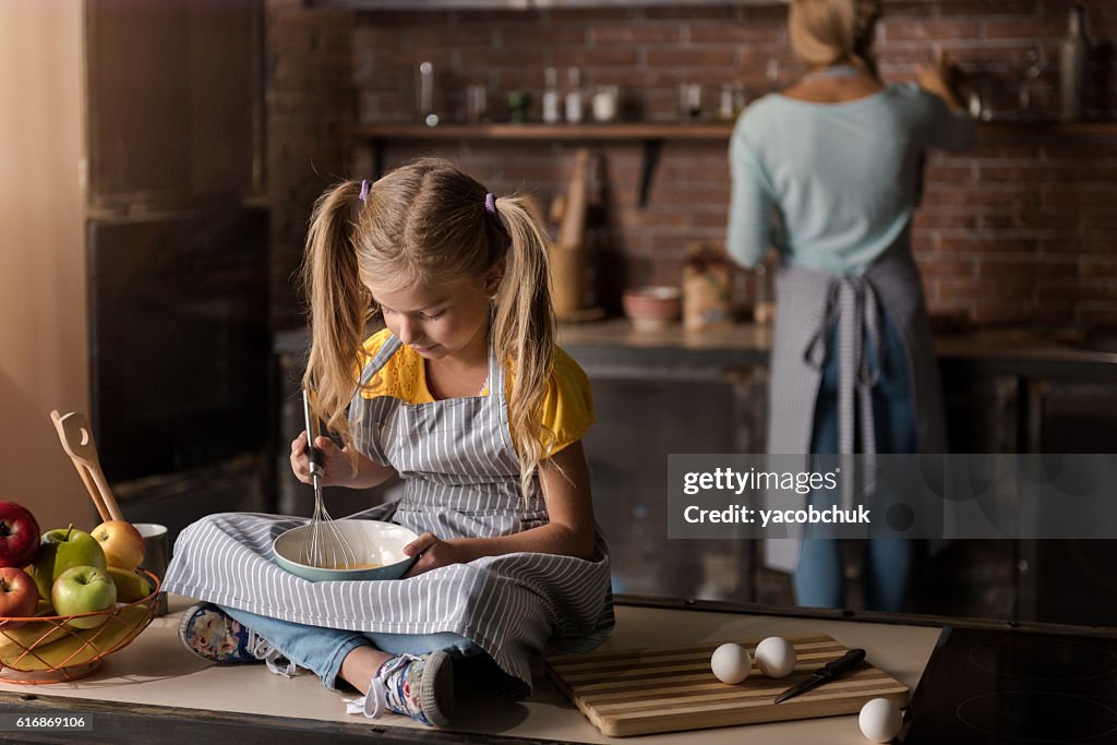 Involved girl mixing eggs sitting on the table