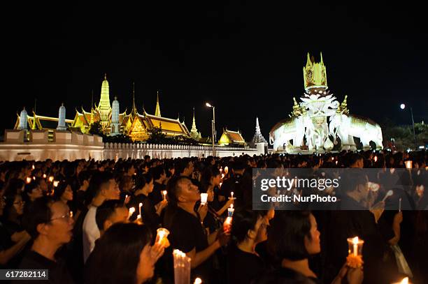 Mourners hold candles as they gather outside of the Grand Palace to sing for a recording of the royal anthem in honour of Thailand's late King...