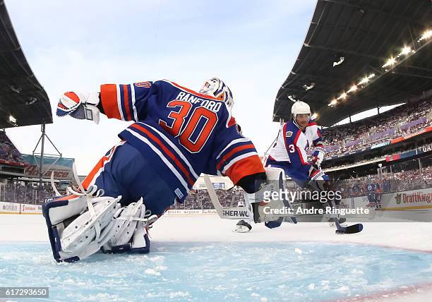 Teemu Selanne of the Winnipeg Jets alumni stickhandles the puck in on Bill Ranford of the Edmonton Oilers alumni to score a first period goal during...