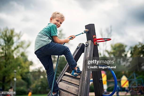 kleiner junge klettert auf dem spielplatz - kinderspielplatz stock-fotos und bilder