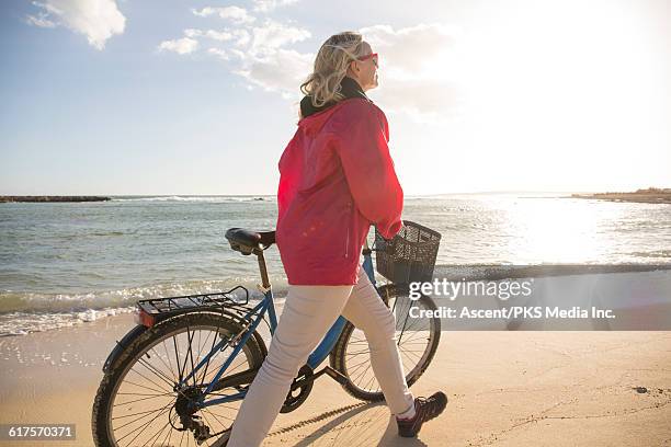 woman pushes bike along sandy beach, sunrise - red coat stock pictures, royalty-free photos & images