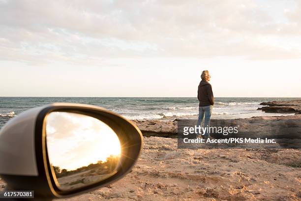 view past car mirror as man walks onto tidal rocks - car back view bildbanksfoton och bilder