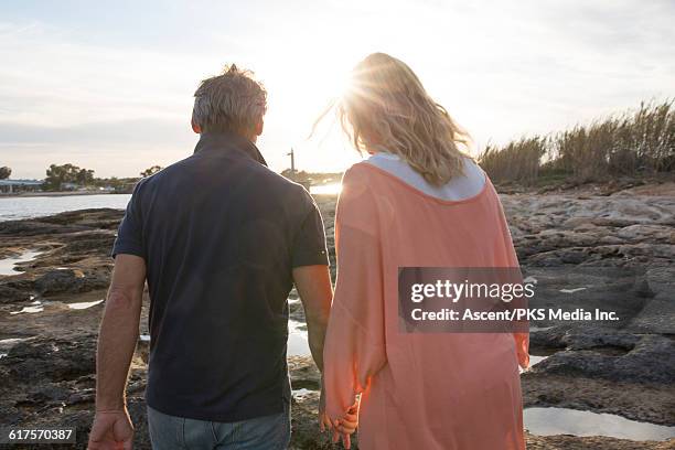 couple walk across tidal flat towards sunrise - woman finding grey hair stock pictures, royalty-free photos & images