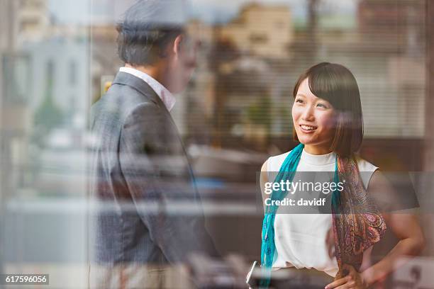 japanese business man and woman meeting viewed through office window - rijk stockfoto's en -beelden