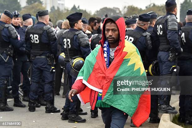 Migrant from Ethiopia with the Oromo Liberation Front flag on his shoulders walks past French anti-riot police during the full evacuation of the...