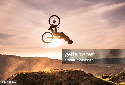 Geschickter Radfahrer, der bei Sonnenuntergang Backflip gegen den Himmel macht. Geschickter Radfahrer, der bei Sonnenuntergang Backflip gegen den Himmel macht.