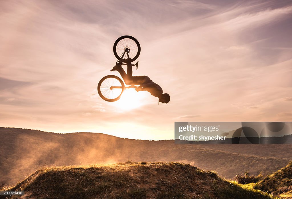 Hábil ciclista haciendo backflip contra el cielo al atardecer.