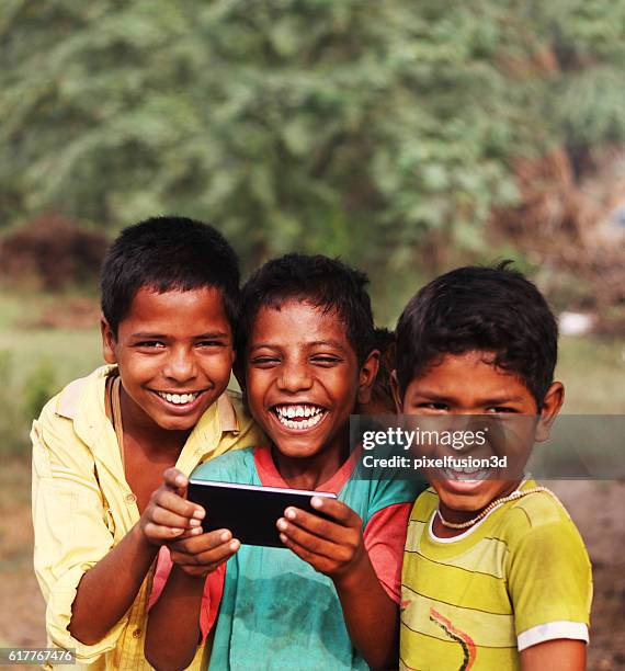 niños rurales alegres sosteniendo teléfonos inteligentes - indian slums fotografías e imágenes de stock