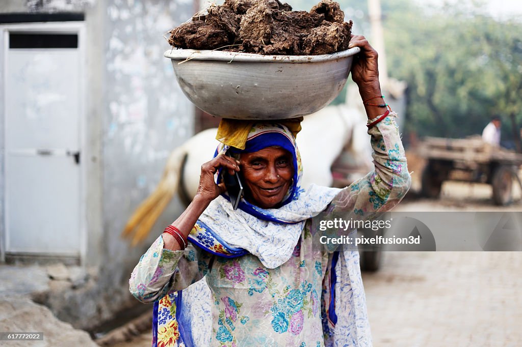 Old women carrying cow dung and talking on phone