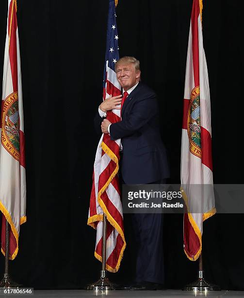 Republican presidential candidate Donald Trump hugs the American flag as he arrives for a campaign rally at the MidFlorida Credit Union Amphitheatre...