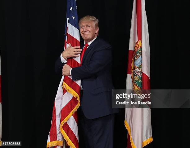 Republican presidential candidate Donald Trump hugs the American flag as he arrives for a campaign rally at the MidFlorida Credit Union Amphitheatre...