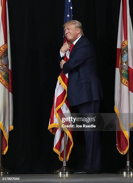 Republican presidential candidate Donald Trump hugs the American flag as he arrives for a campaign rally at the MidFlorida Credit Union Amphitheatre...