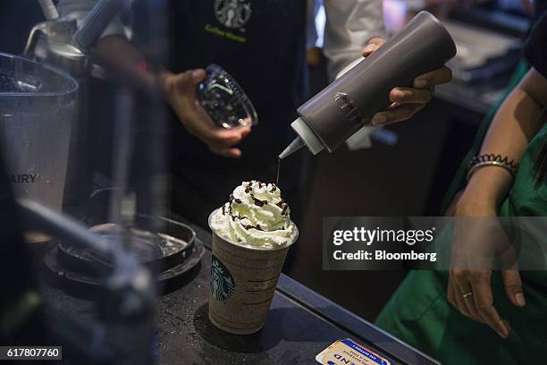 An employee pours syrup over whipped cream while preparing a coffee drink at a Starbucks Corp. Coffee shop in Phnom Penh, Cambodia on Monday, Oct....