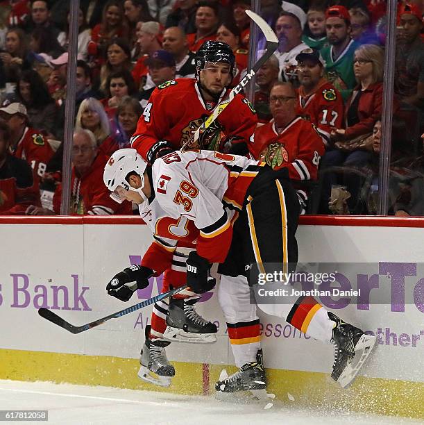 Alex Chiasson of the Calgary Flames checks Niklas Hjalmarsson of the Chicago Blackhawks into the boards at the United Center on October 24, 2016 in...