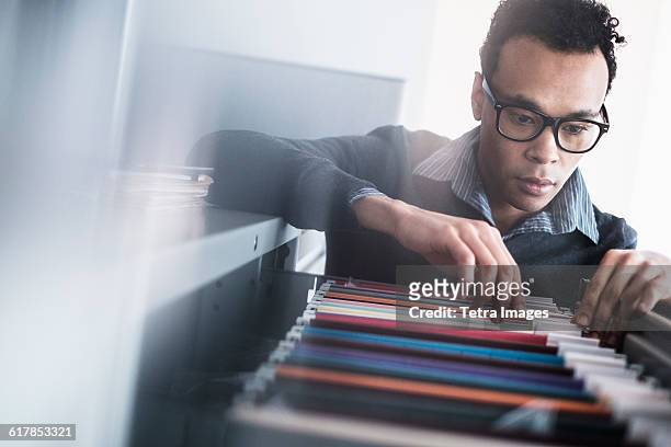 mid adult man searching for files in filing cabinet - filing cabinet photos et images de collection