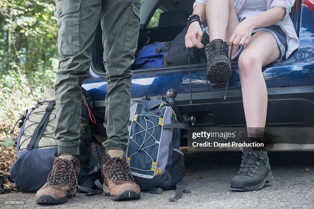 "Young woman sitting in car boot and putting on her hiking shoes, Bavaria, Germany"