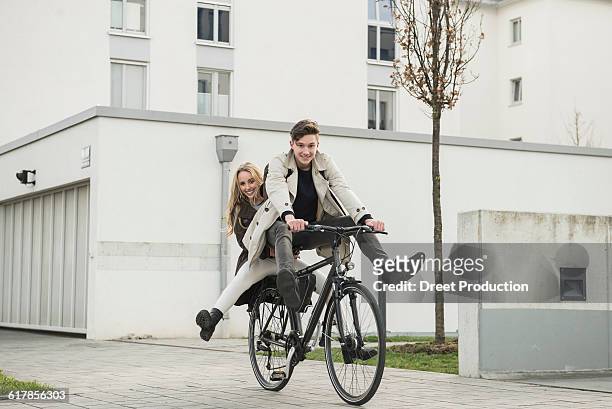 "young couple riding a cycle on street, munich, bavaria, germany" - bavaria girl stockfoto's en -beelden