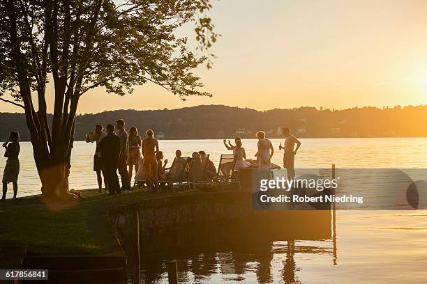 "group of young friends partying at lakeside during sunset, bavaria, germany" - riva del lago foto e immagini stock