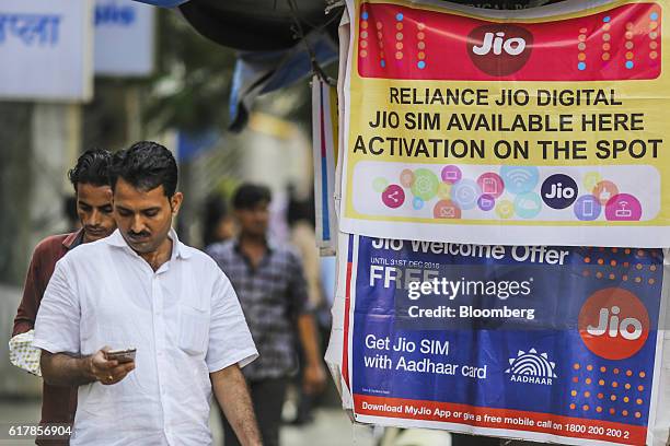 Pedestrian using a mobile phone walks past banners for Reliance Jio, the mobile network of Reliance Industries Ltd., and Bharti Airtel Ltd. Outside a...