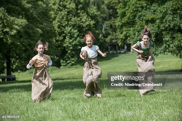 "three girls jumping in sack race in a field, munich, bavaria, germany" - sack race stock pictures, royalty-free photos & images