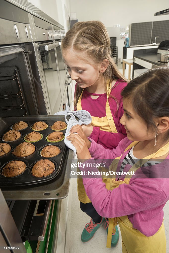 "Schoolgirls removing muffins from oven in home economics class, Bavaria, Germany"