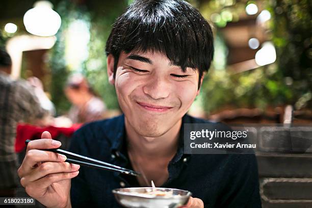 funny young japanese man eating using chopsticks - japanese chopsticks stock pictures, royalty-free photos & images