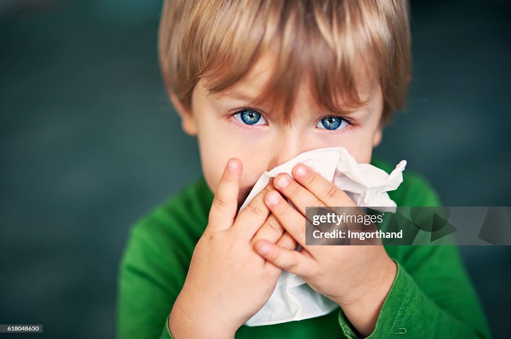 Retrato de un niño enfermo limpiándose la nariz