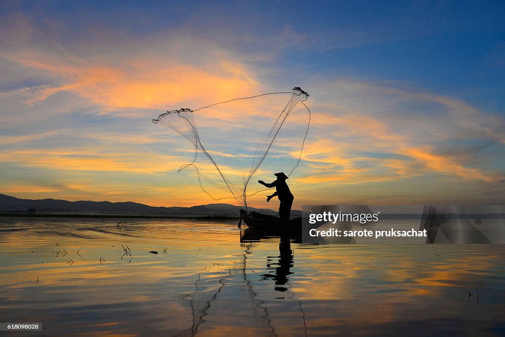 Silhouette of traditional fishermen throwing net fishing at sunrise time.