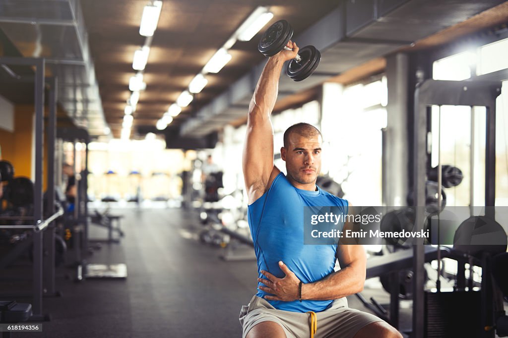 Young muscular man lifting up dumbbells at the gym.