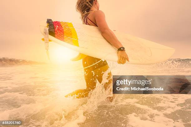 low angle women surfer running into the ocean at sunset - california beach surf stock pictures, royalty-free photos & images