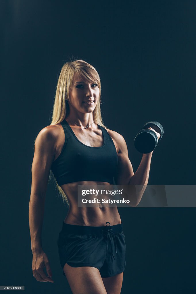 Athletic woman with dumbbells on a dark background