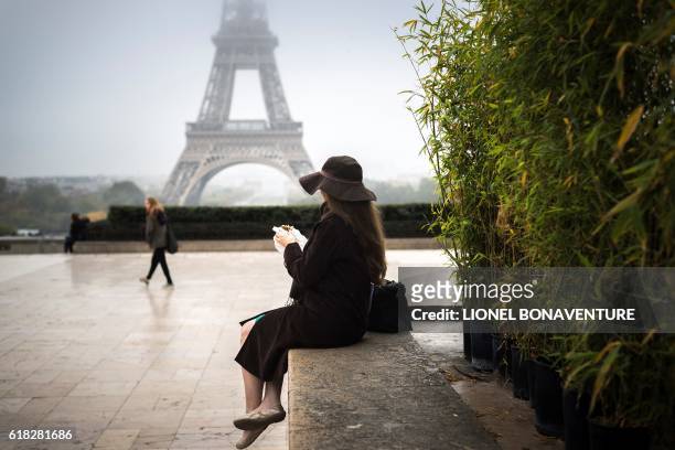 Woman sits on a stone ledge on the Parvis des droits de l'homme square, in front of the Eiffel tower, on October 26, 2016 in Paris.