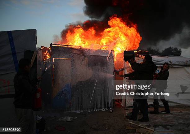 Volunteers and migrants tackle a blaze in the Jungle camp as authorities demolish the site on October 26, 2016 in Calais, France. Overnight fires...