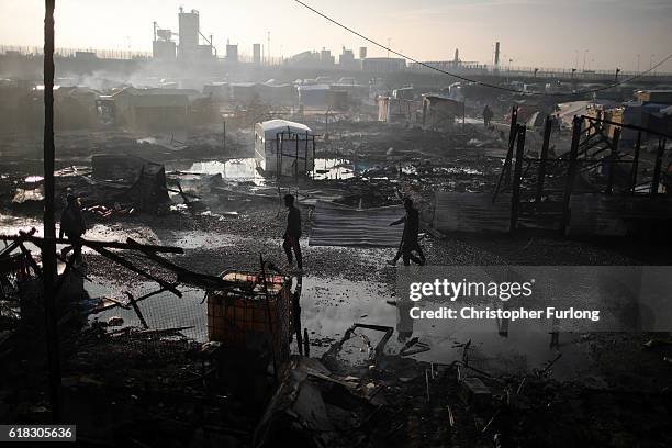 Migrants walk through the burnt out Jungle camp as authorities demolish the site on October 26, 2016 in Calais, France. Overnight fires broke out in...